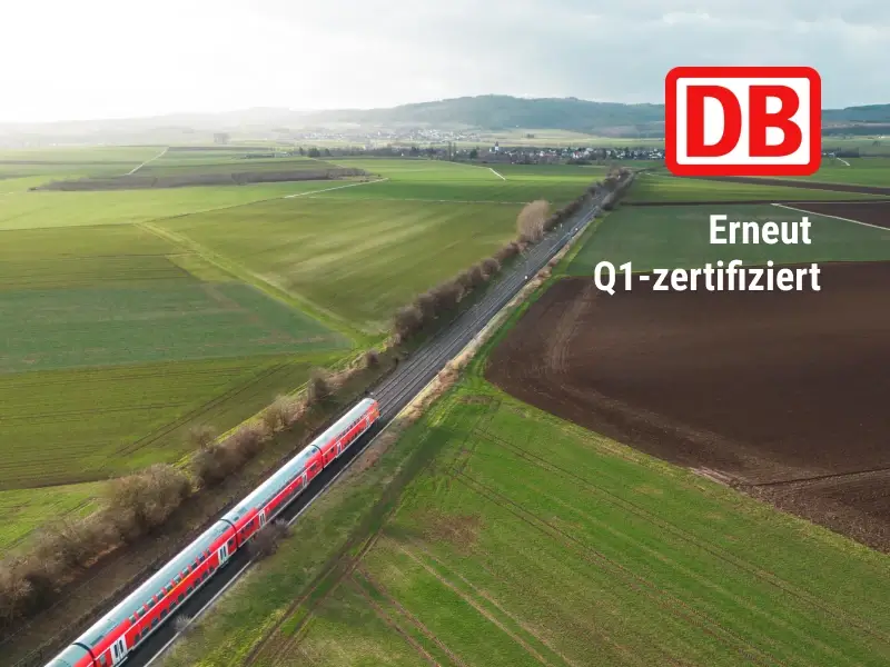 Bild eines rot-weißen Zuges, der durch eine ländliche Landschaft fährt, mit DB Logo und Text WErneut Q1-zertifiziert"