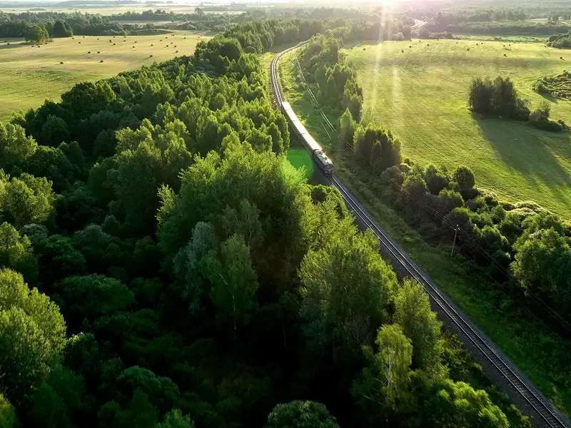 Luftaufnahme einer Bahnstrecke, die sich durch eine grüne Wald- und Wiesenlandschaft zieht